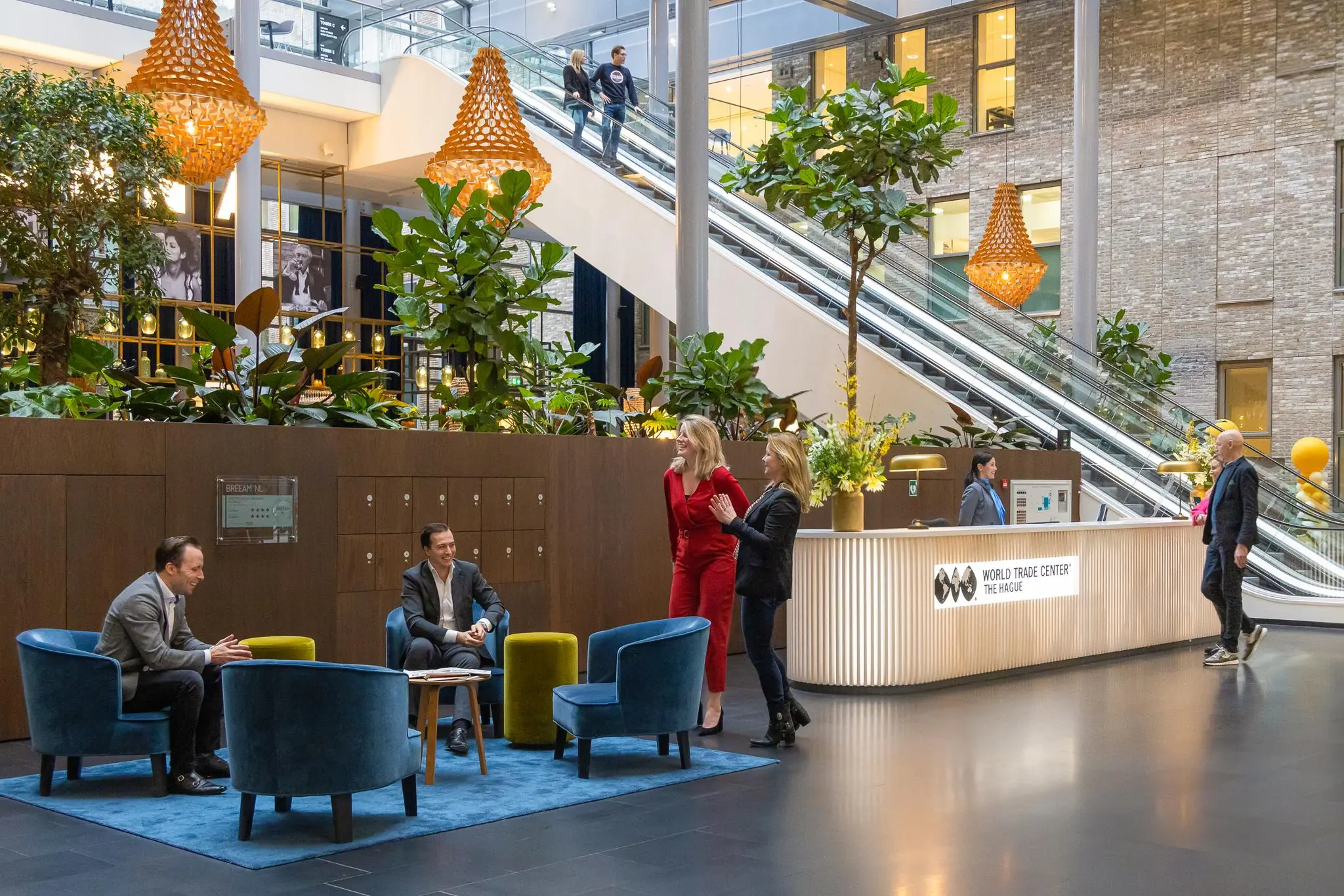 Moderne ontvangsthal van het World Trade Center Den Haag aan de Prinses Beatrixlaan met mensen in gesprek en een opvallende groene inrichting.